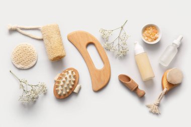 Ahşap guasha vücut masajı aracı ve gri arka planda farklı banyo malzemeleri ile kompozisyon