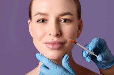 Güzel genç bir kadın mor arka planda yüzüne iğne vuruluyor. Yakın plan.