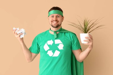 Çevreci süper kahraman gibi giyinmiş genç bir adam. Ev bitkisi ve bej arka planda çöp. Ekoloji kavramı