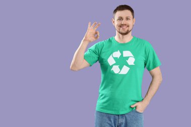 Geri dönüşüm logosu olan mutlu genç adam leylak arka planda iyi görünüyor. Ekoloji kavramı