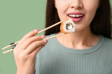 Genç Asyalı kadın yeşil arka planda çubukları olan lezzetli suşi rulosu tutuyor, yakın plan.