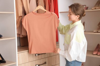 Evde gardıropta asılı tişörtlü bir kadın var.