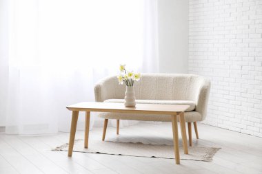 Beyaz oturma odasında rahat bir kanepe, masa ve ışık perdeleri.