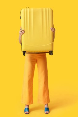 Sarı arka planda bavulu olan genç bir kadın. Seyahat kavramı
