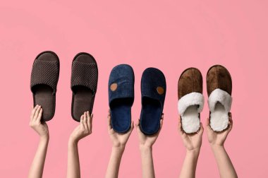 Pembe arka planda farklı erkek terlikleri tutan kadın eller.