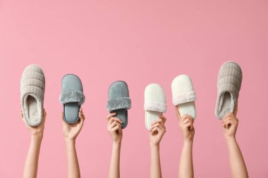 Pembe arka planda farklı kadınların terliklerini tutan kadın elleri.