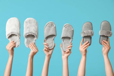 Mavi arka planda farklı terlikler tutan kadın eller.