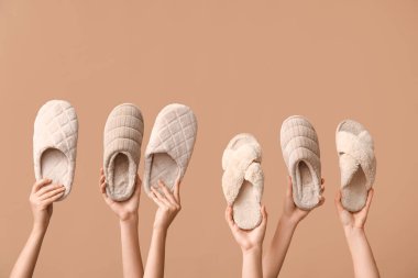 Bej arka planda farklı terlikler tutan kadın eller.