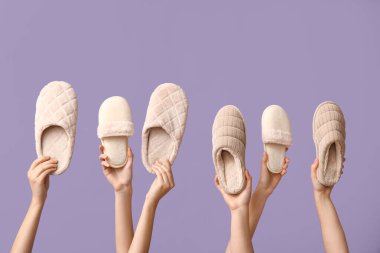 Leylak arka planında farklı terlikler tutan kadın eller.