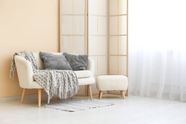 Odadaki ışık perdesinin yanında ekose ve minderli rahat bir kanepe.