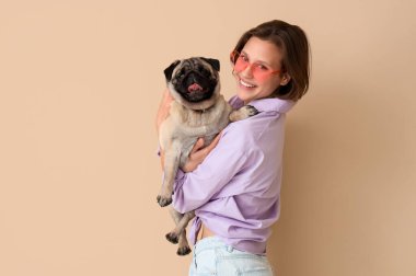 Bej arka planda sevimli köpekli genç bir kadın.