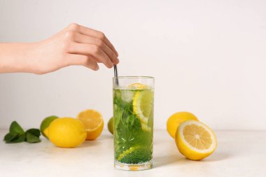 Beyaz arka planda bir bardak limonata, limon ve saman olan bir kadın eli.