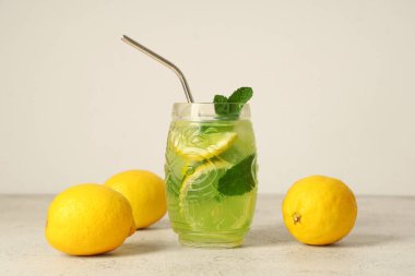 Bir bardak limonlu lezzetli limonata ve beyaz arka planda saman.