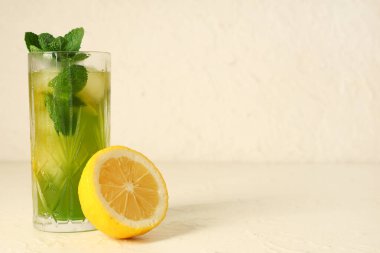 Bir bardak limonata, dilimlenmiş limon ve naneli beyaz arka plan.