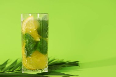 Limon dilimli bir bardak lezzetli limonata ve yeşil arkaplanda nane.