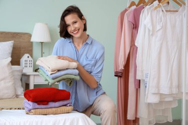 Genç ve güzel bir kadın, evde katlanan elbiseleri katlıyor.