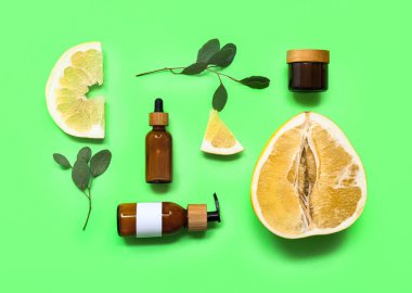 Yeşil zemin üzerinde kozmetik ürün şişeleri, yapraklar ve taze pomelo ile güzel bir kompozisyon