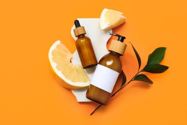 Turuncu arka planda kozmetik ürünler, yapraklar ve taze zeytin parçaları.