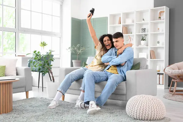 Happy young couple playing video games on sofa at home