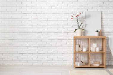 Beyaz tuğla duvarın yanında banyo aksesuarları olan raf ünitesi.