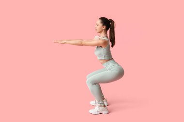 Genç bayan antrenör pembe arka plan üzerinde egzersiz yapıyor.