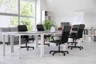 Büyük masası, koltukları, raf ünitesi ve saksısı olan modern konferans salonu.
