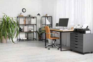 Çalışma yeri, bilgisayar, çekmece sandığı ve raf ünitesi olan modern ofis.