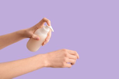 Leylak arka planına kozmetik ürünler uygulayan kadın eller