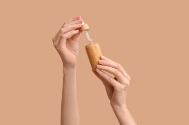 Kahverengi arka planda kozmetik ürünü şişesi olan kadın elleri