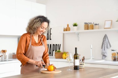 Evinde portakal kesen bir şişe ve bir bardak şarapla orta yaşlı güzel bir kadın.
