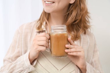 Elinde kavanoz dolusu lezzetli buzlu latte olan genç bir kadın.