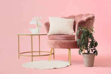 Ev bitkisi, kahve masası ve pembe arka planda halı olan güzel bir koltuk.
