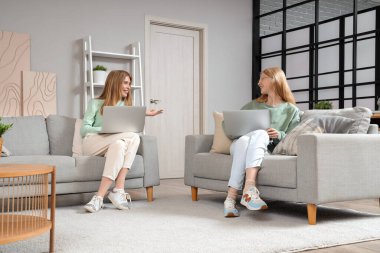 Evdeki kanepede dizüstü bilgisayarı olan güzel, mutlu kız kardeşler.