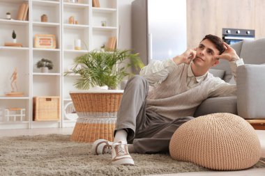 Evdeki kanepenin yanında cep telefonuyla konuşan genç bir adam.