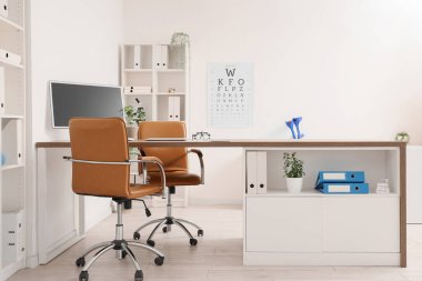 Doktorun çalışma yeri ve göz testi çizelgesi bulunan bir sağlık bürosu.