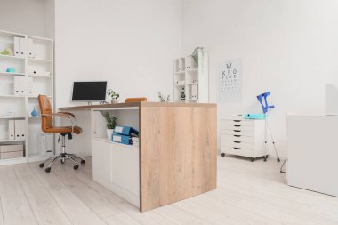 Doktorun iş yeri, raf üniteleri ve göz testi çizelgesi bulunan sağlık bürosu.