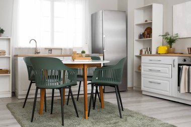 Buzdolabı olan aydınlık mutfağın içi, fırını ve yemek masası olan beyaz tezgahlar.