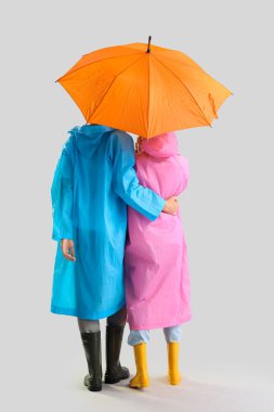 Arka planda şemsiyesi olan yağmurluk giymiş genç bir çift.