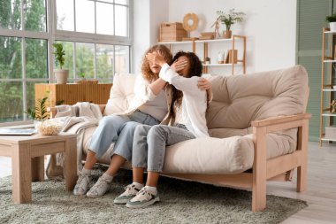 Evdeki kanepede gözlerini kapayan genç kadınlar.