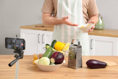 Taze sebzeli genç adam mutfakta yemek pişirme videosu kaydediyor.