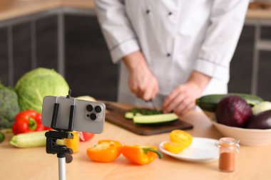 Taze sebzeli erkek şef mutfaktaki cep telefonundan yemek pişirme videosu kaydediyor.