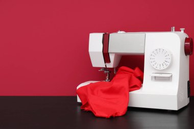 Kırmızı arka planda kumaşı olan modern dikiş makinesi