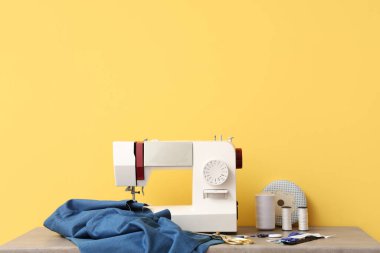 Sarı arka planda kumaş ve terzi malzemesi olan modern dikiş makinesi.
