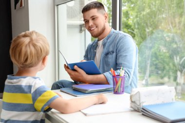 Genç adam evde oğluyla ödev yapıyor.