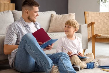 Genç adam ve küçük oğlu oturma odasında yerde otururken ödev yapıyorlar.
