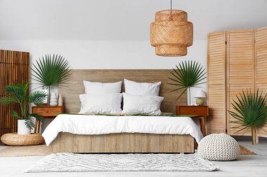 Büyük yatak, komodin ve yatak odasındaki palmiye dallarıyla süslenmiş katlanmış ekran.