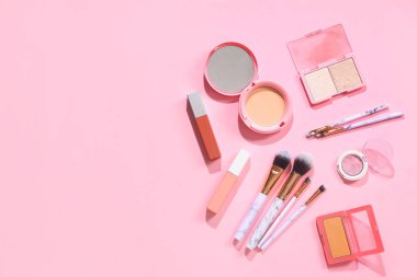 Pembe arka planda kozmetik ürünlerle süslü makyaj fırçaları