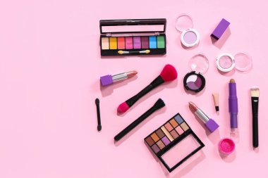 Pembe arka planda kozmetik ürünlerle süslü makyaj fırçaları