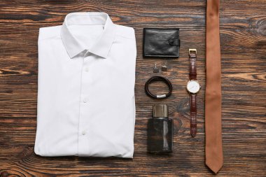 Ahşap arka planda parfüm şişesi, cüzdanı ve aksesuarları olan erkek gömleği.