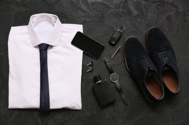 Siyah arka planda gömlekli, cep telefonlu ve ayakkabılı erkek aksesuarları. Üst görünüm